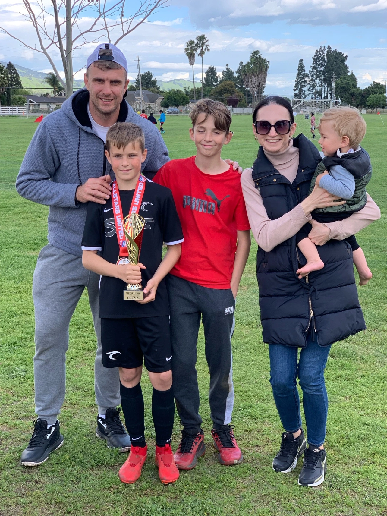 Family celebrating with a soccer trophy outdoors.